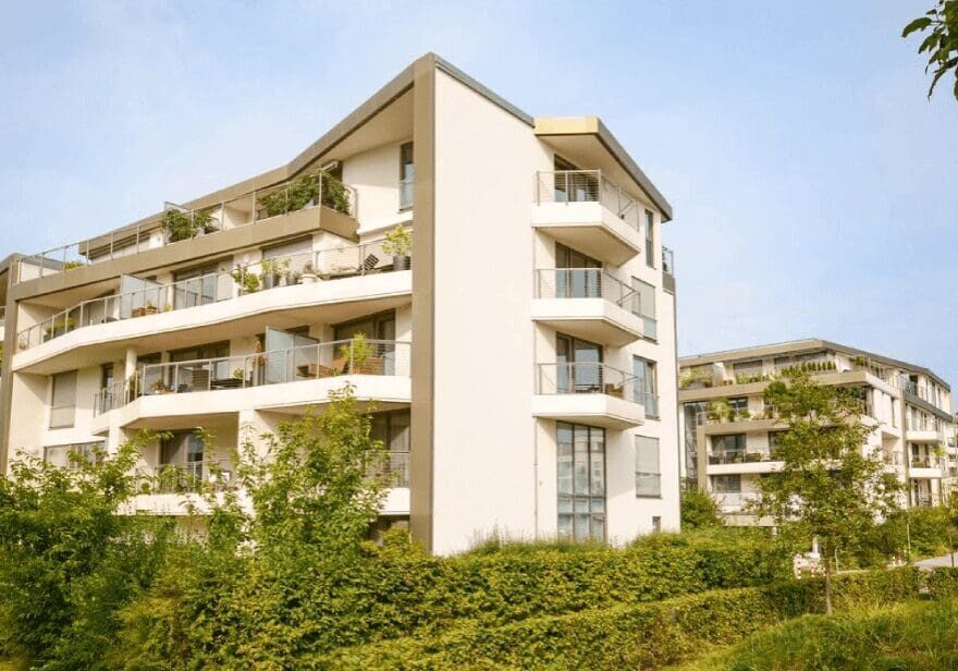 A large white building with many balconies and trees.